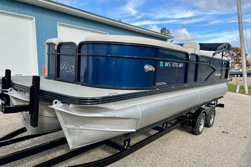 Slide: The Image of 2018 Manitou 23 Aurora LE pontoon boat on trailer, parked near blue building. - 54
