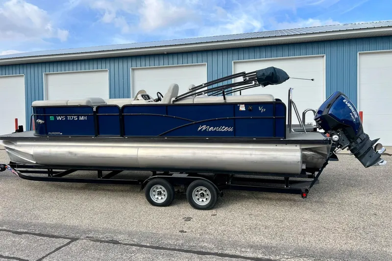Slide: The Image of 2018 Manitou 23 Aurora LE pontoon boat on trailer, parked near blue building. - 57