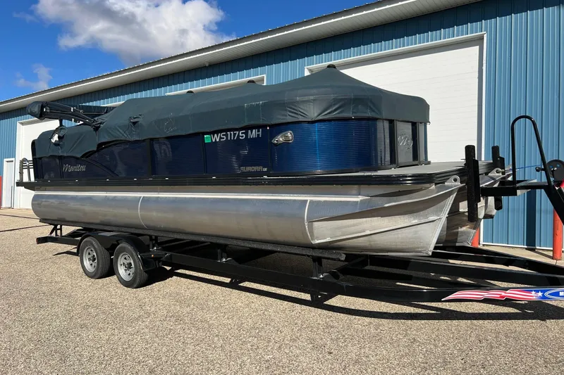 Slide: The Image of 2018 Manitou 23 Aurora LE pontoon boat on trailer, covered, near blue building. - 60