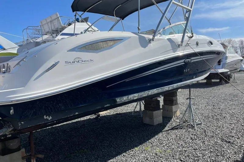 Slide: The Image of 2012 Sea Ray 300 Sundeck boat on stands, blue and white exterior, sunny day. - 3