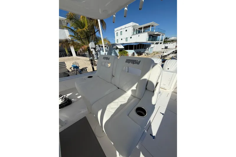 Slide: The Image of 2014 Intrepid 327 Center Console boat with white seating and cup holder, docked near modern homes. - 24