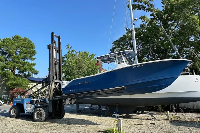 Slide: The Image of 2023 NauticStar 28 XS boat lifted by forklift, surrounded by trees. - 2