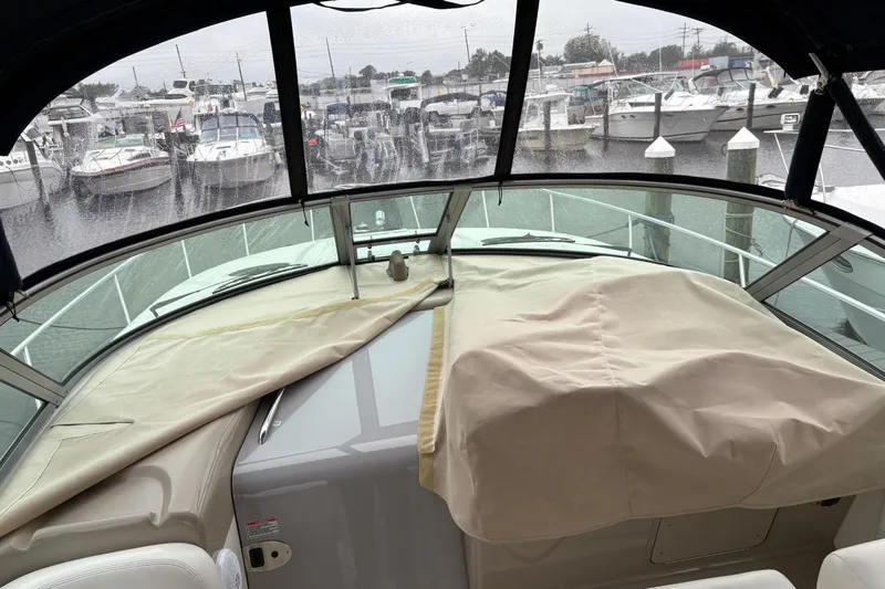 Slide: The Image of 2003 Sea Ray 320 Sundancer cockpit view with covered dashboard, marina background. - 56