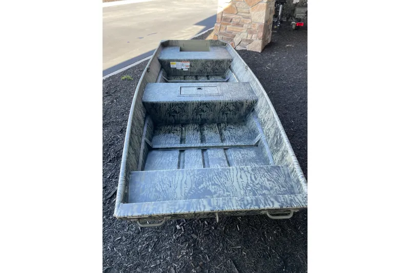 Slide: The Image of 2026 Tracker Grizzly 15 Jon boat with camouflage design, parked on a paved surface. - 2