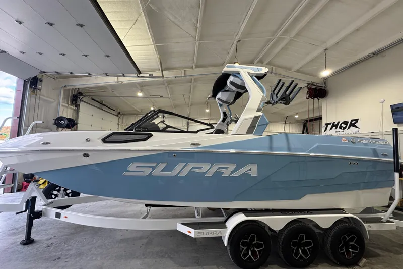 The Image of 2026 Supra SE boat in a garage, featuring a sleek blue and white design. - 3