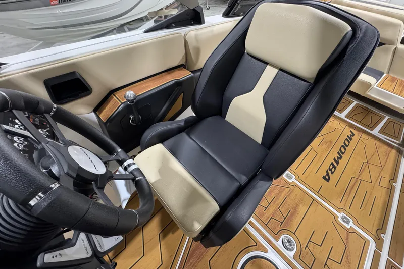 Slide: The Image of 2026 Moomba Mojo boat interior with black and beige seating, steering wheel, and wood-patterned flooring. - 16