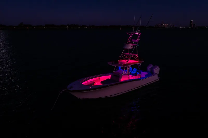 Slide: The Image of 2019 Mag Bay 33 CC boat illuminated with vibrant pink and blue lights at night. - 16