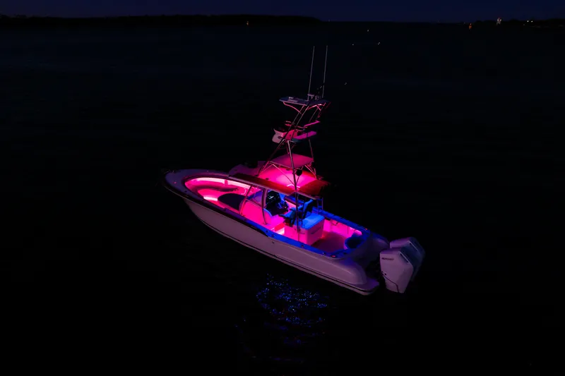 Slide: The Image of 2019 Mag Bay 33 CC boat illuminated with vibrant pink and blue lights at night. - 18