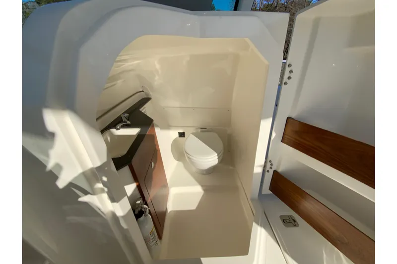 Slide: The Image of 2026 Pursuit DC 246 Dual Console boat interior with compact bathroom and wooden accents. - 36
