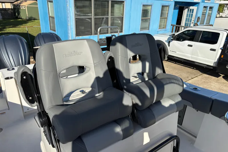 Slide: The Image of 2023 NauticStar 28 XS boat seats with gray upholstery, parked near a blue building. - 20