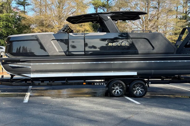 Slide: The Image of 2026 Revel RS25L luxury boat on trailer in parking lot, surrounded by trees. - 23