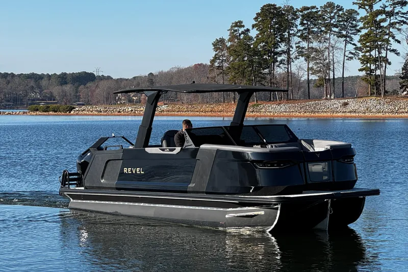 Slide: The Image of Revel RS25L 2026 boat cruising on a serene lake with scenic forest backdrop. - 8