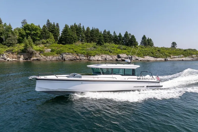 Slide: The Image of 2026 Axopar 37 XC cruising near a scenic, forested shoreline. - 7