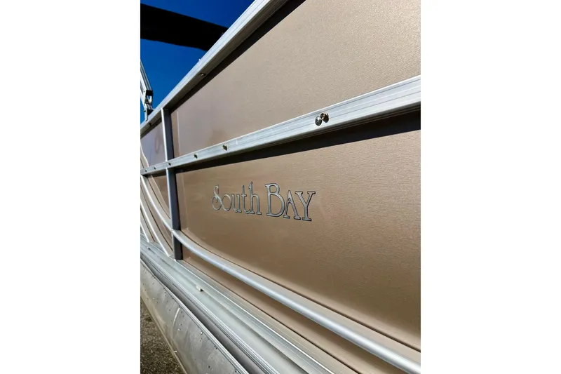Slide: The Image of 2013 South Bay 417 CR pontoon boat with beige seating, parked near blue building. - 3