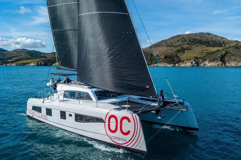 Slide: The Image of 2026 Catana OC2 catamaran sailing in clear blue waters near a scenic coastline. - 2