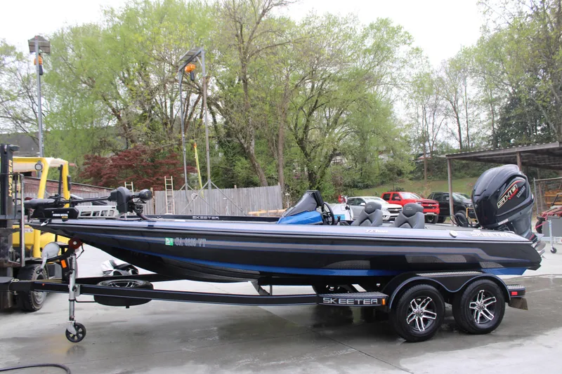 The Image of 2022 Skeeter ZX225 bass boat on trailer, parked outdoors with trees in background. - 1