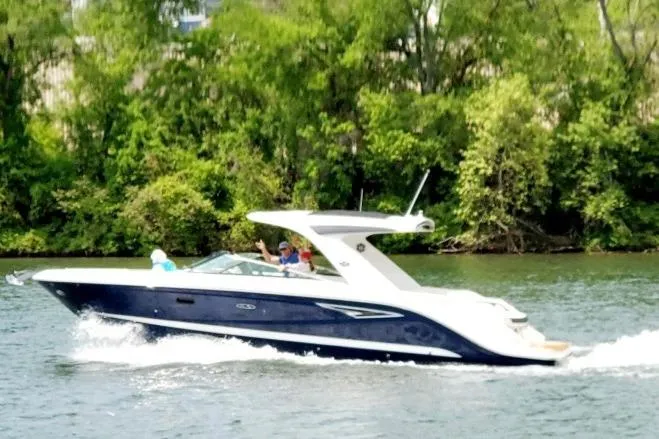 Slide: The Image of 2023 Sea Ray SLX 310 cruising on a scenic river with lush green trees. - 2