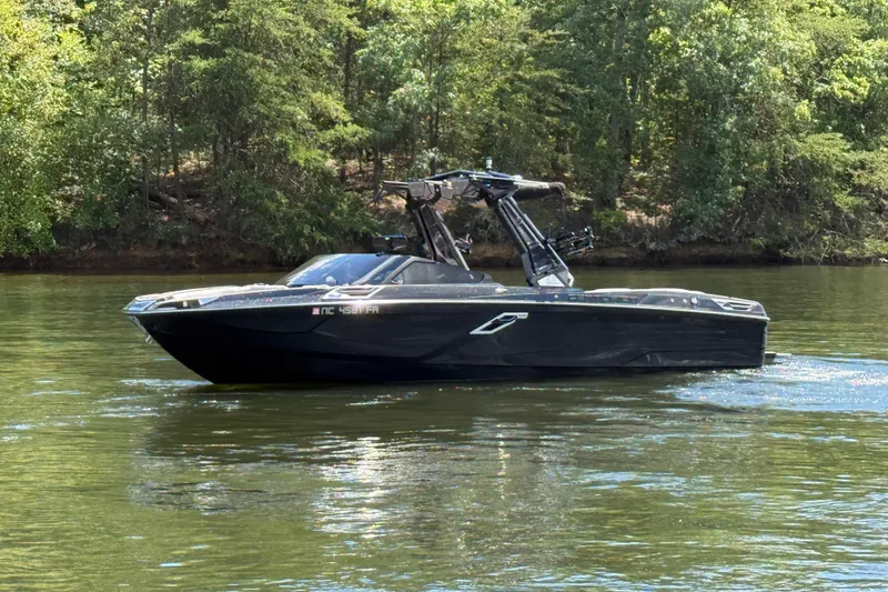 Slide: The Image of 2023 Centurion Ri265 boat cruising on a serene lake with lush green forest backdrop. - 4