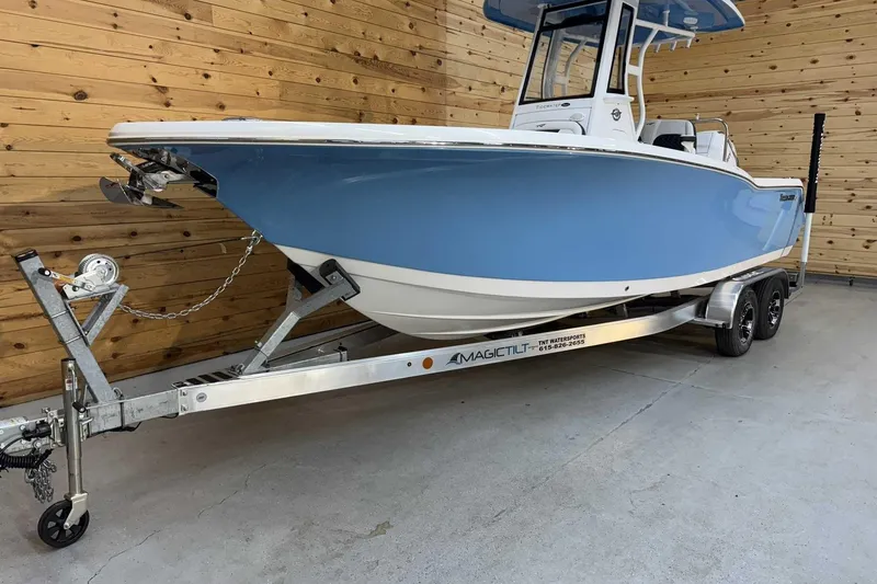 Slide: The Image of 2025 Tidewater 232 CC Adventure boat on trailer, blue hull, wooden background. - 6