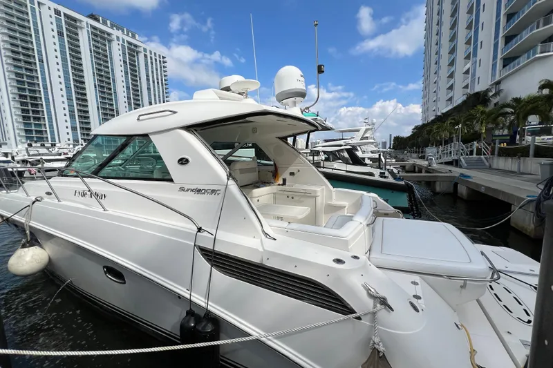 The Image of 2010 Sea Ray 450 Sundancer yacht docked at marina, surrounded by modern buildings. - 0