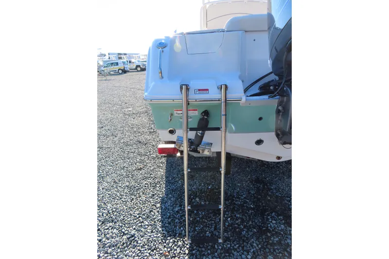 Slide: The Image of 2023 Sea Hunt Ultra 234 boat with rear ladder and motor, parked on gravel. - 6