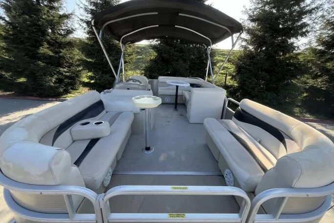 Slide: The Image of 2013 Godfry Sweetwater pontoon boat with beige seating and canopy, surrounded by trees. - 12