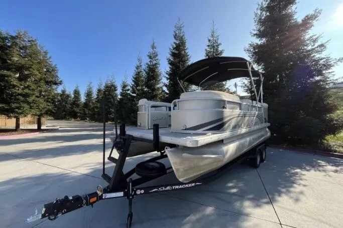 Slide: The Image of 2013 Godfry Sweetwater pontoon boat on trailer, surrounded by trees, under clear sky. - 6