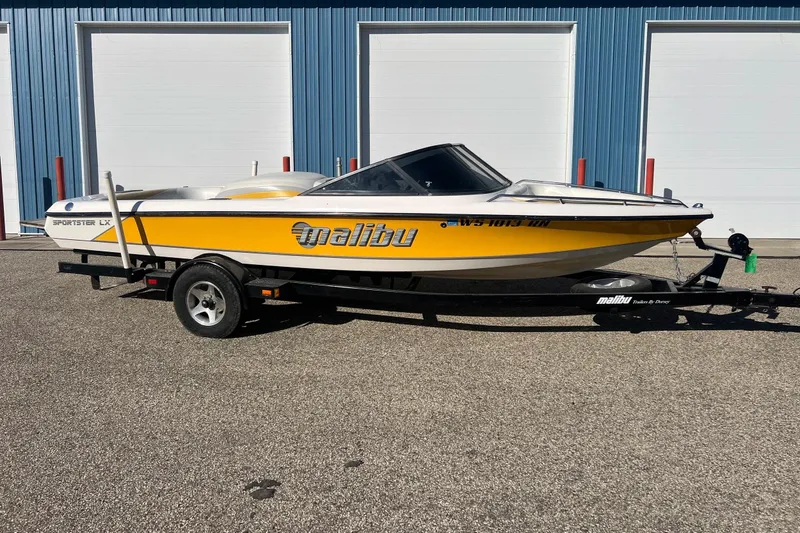 Slide: The Image of 2002 Malibu Sportster LX boat on trailer, parked outside blue building. - 1
