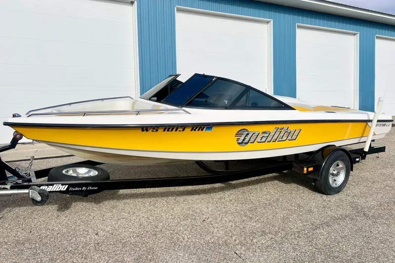 Slide: The Image of 2002 Malibu Sportster LX boat in yellow, parked on a trailer near blue building. - 36