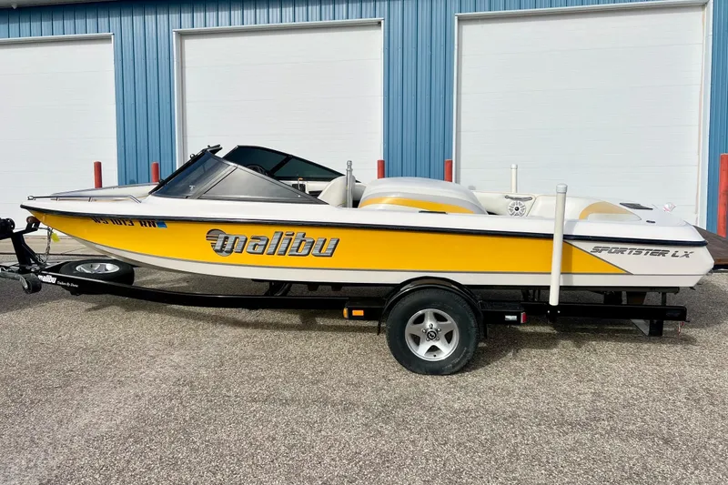 Slide: The Image of 2002 Malibu Sportster LX boat in yellow, parked on a trailer near blue building. - 37