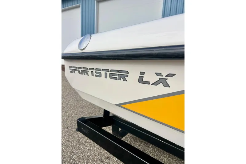 Slide: The Image of 2002 Malibu Sportster LX boat with yellow accent, parked near a blue building. - 4