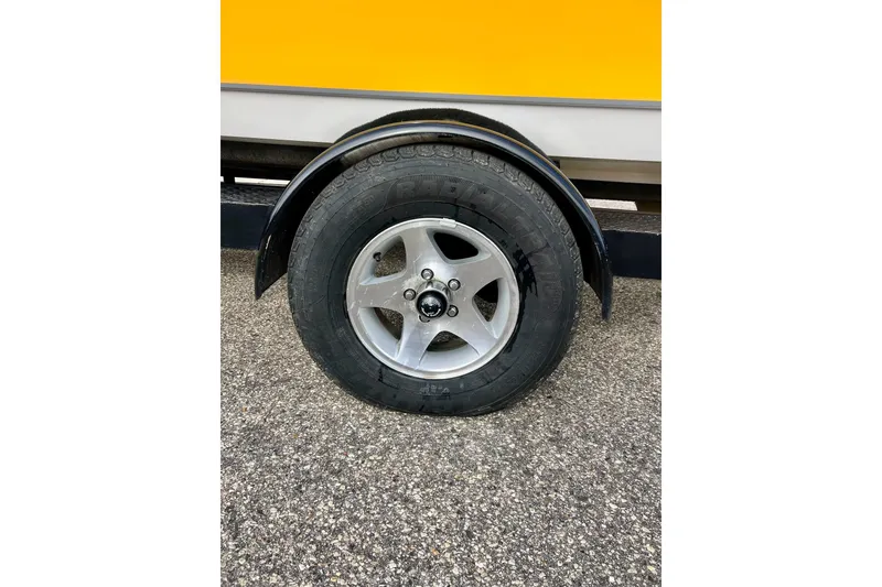 Slide: The Image of 2002 Malibu Sportster LX trailer wheel on asphalt, featuring a black fender and silver rim. - 5