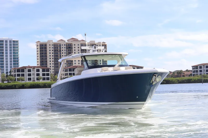 Slide: The Image of 2023 Tiara Yachts 43 LS cruising on a scenic waterway with buildings in the background. - 2