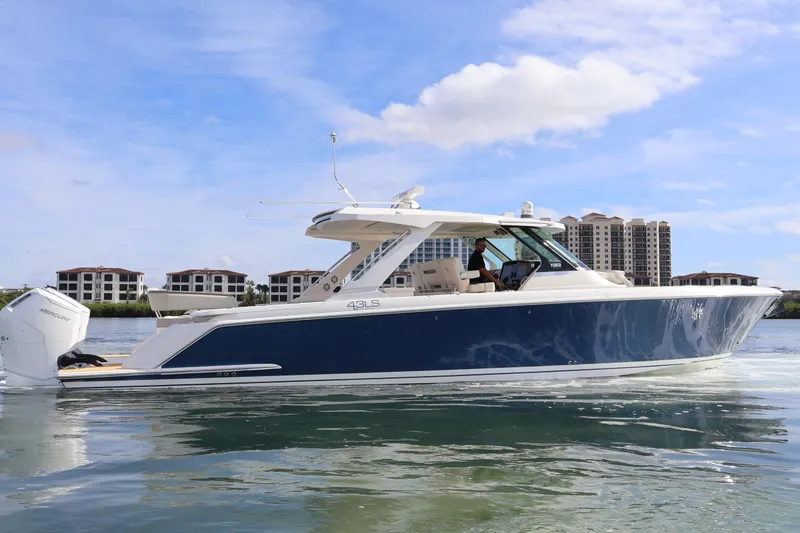 Slide: The Image of 2023 Tiara Yachts 43 LS cruising on calm waters, with modern buildings in the background. - 3