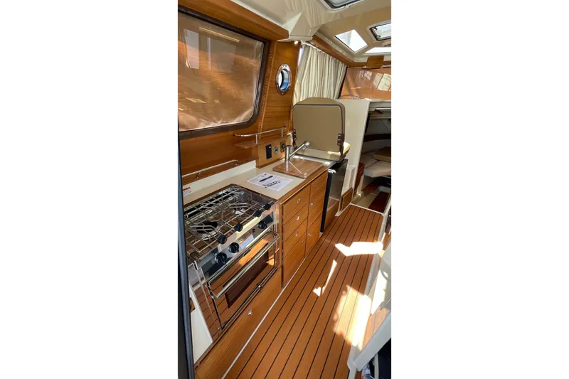 Slide: The Image of 2025 Ranger Tugs R-27 Seakeeper Ride interior with wood finish and compact kitchen. - 30