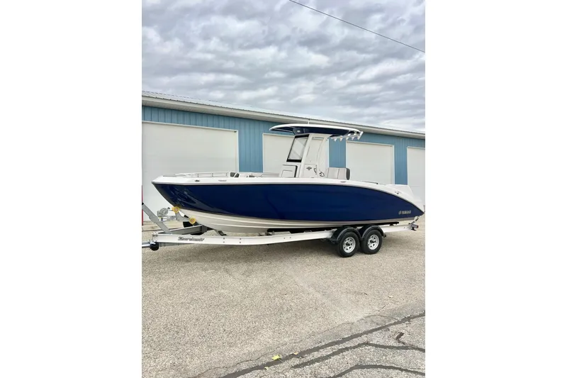 Slide: The Image of 2022 Yamaha Boats 255 FSH Sport H, blue hull, on trailer, parked outdoors. - 85