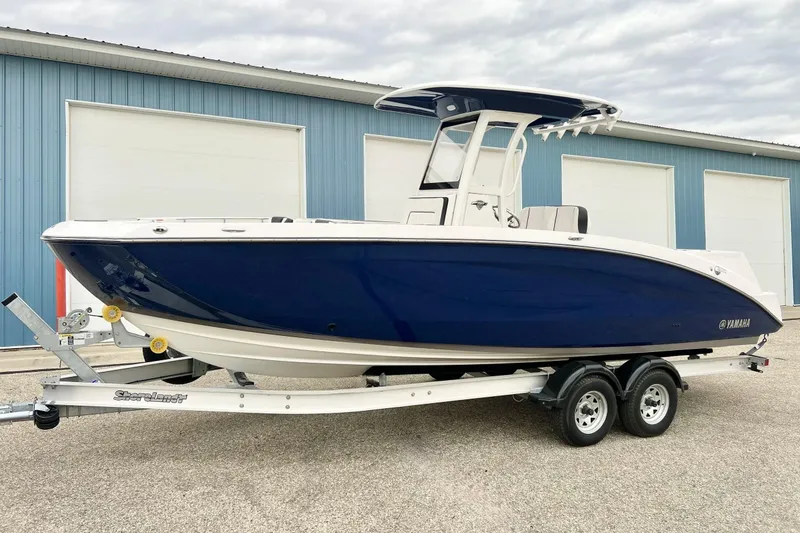 Slide: The Image of 2022 Yamaha Boats 255 FSH Sport H on trailer, blue and white hull, parked outdoors. - 86