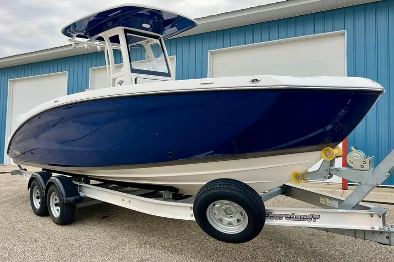 Slide: The Image of 2022 Yamaha Boats 255 FSH Sport H on trailer, blue hull, parked near blue building. - 88