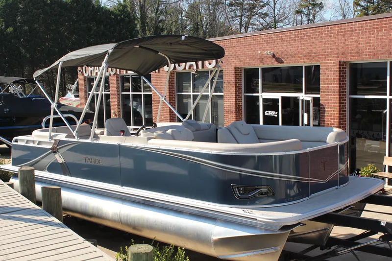 The Image of 2026 Tahoe Pontoon LTZ Elite boat with canopy, docked near a brick building. - 1