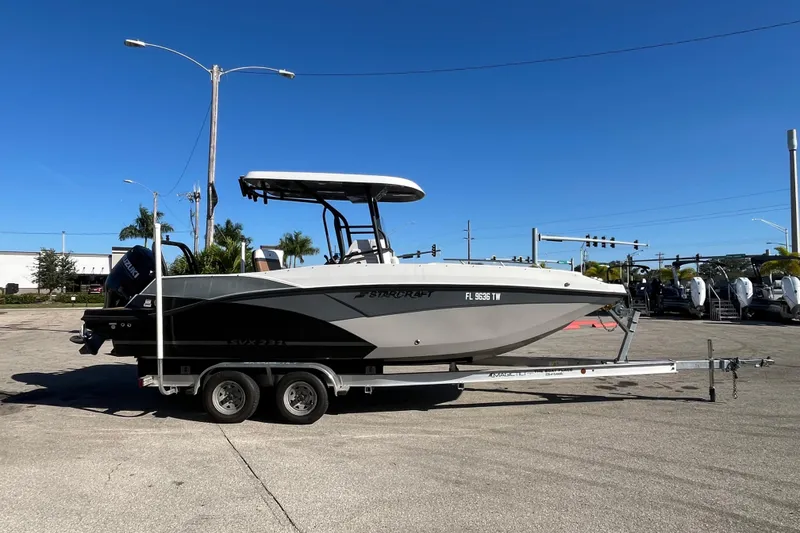 Slide: The Image of 2024 Starcraft SVX 231 OB CC boat on trailer, parked outdoors under clear blue sky. - 3
