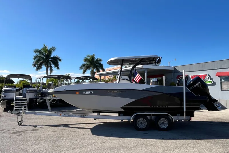 Slide: The Image of 2024 Starcraft SVX 231 OB CC boat on trailer, parked outdoors under clear blue sky. - 7
