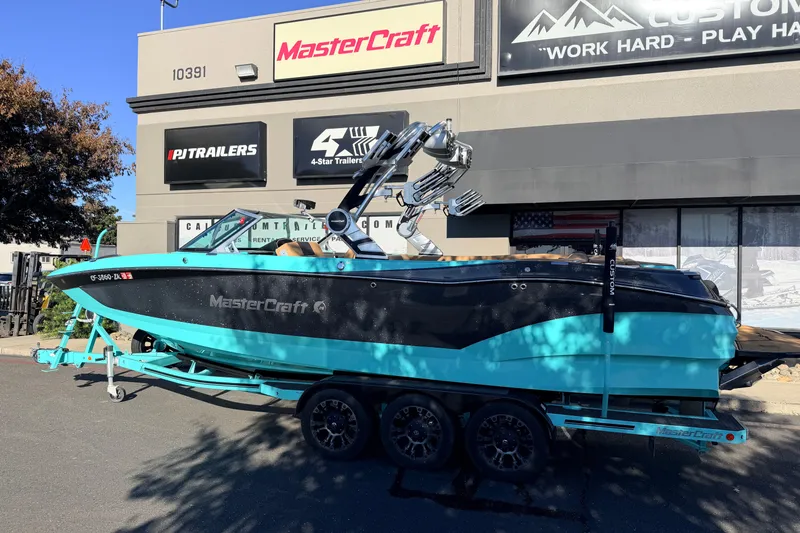 Slide: The Image of 2021 MasterCraft X26 boat in turquoise and black, parked outside dealership. - 8