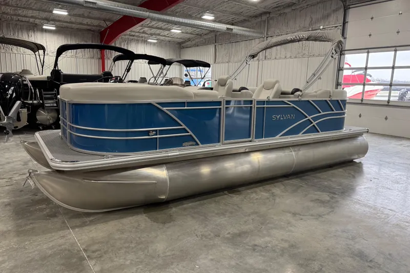 Slide: The Image of 2025 Sylvan 8522 Mirage pontoon boat in showroom, featuring sleek blue design. - 2