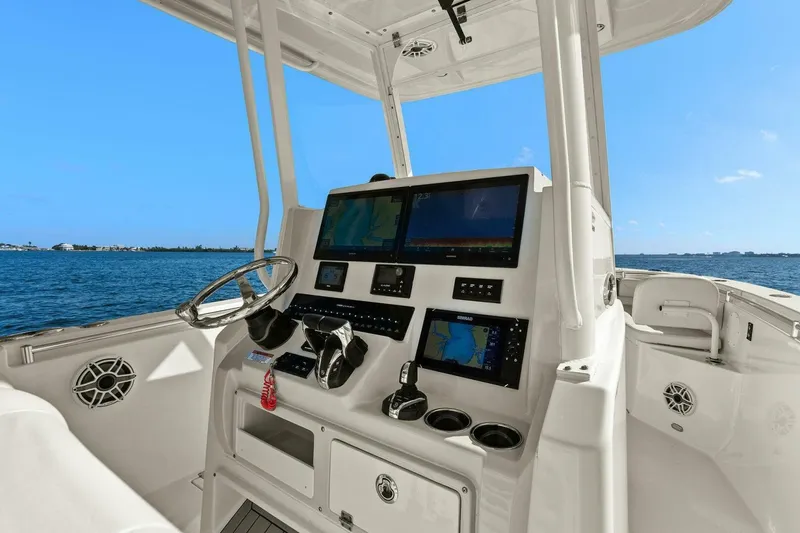 Slide: The Image of 2023 Cobia 301 Center Console boat dashboard with navigation screens, steering wheel, and ocean view. - 17