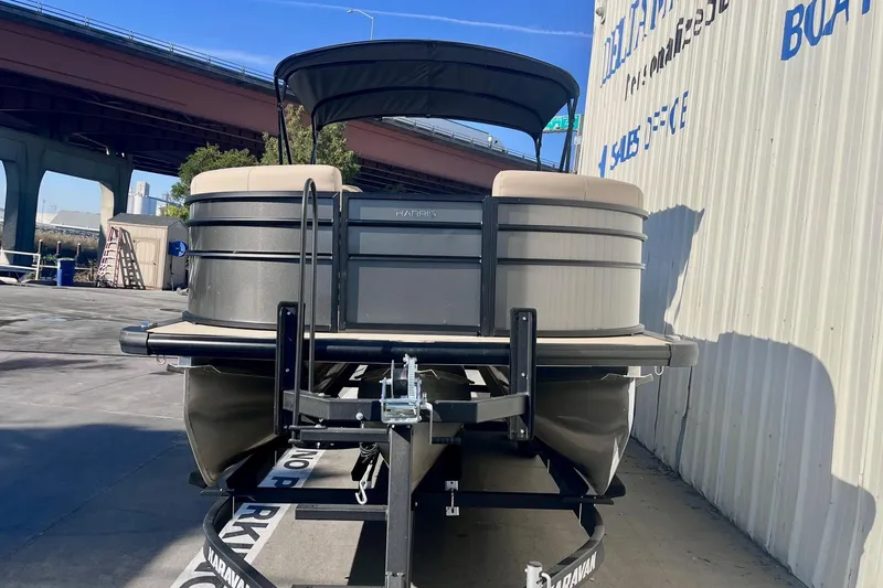 Slide: The Image of 2025 Harris Cruiser 230 pontoon boat on trailer, parked near a building. - 2