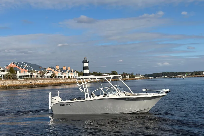 Slide: The Image of 2025 Seapro 240 DLX boat cruising near coastal homes and lighthouse. - 1