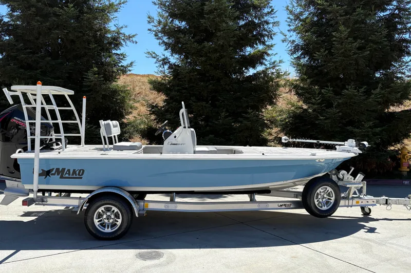 The Image of 2026 Mako 18 Pro Skiff boat on trailer, parked outdoors with trees in background. - 0