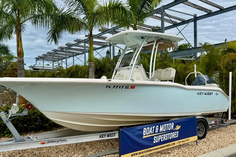 Slide: The Image of 2019 Key West 239 FS boat on trailer at dealership, surrounded by palm trees. - 2