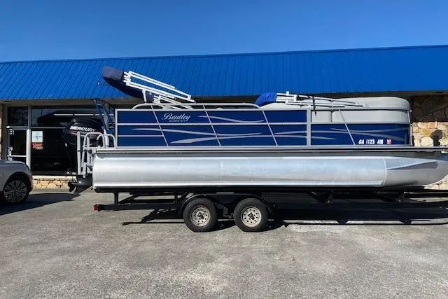 The Image of 2018 Bentley Pontoons 220/223 Cruise boat on trailer, parked outside a blue-roofed building. - 1