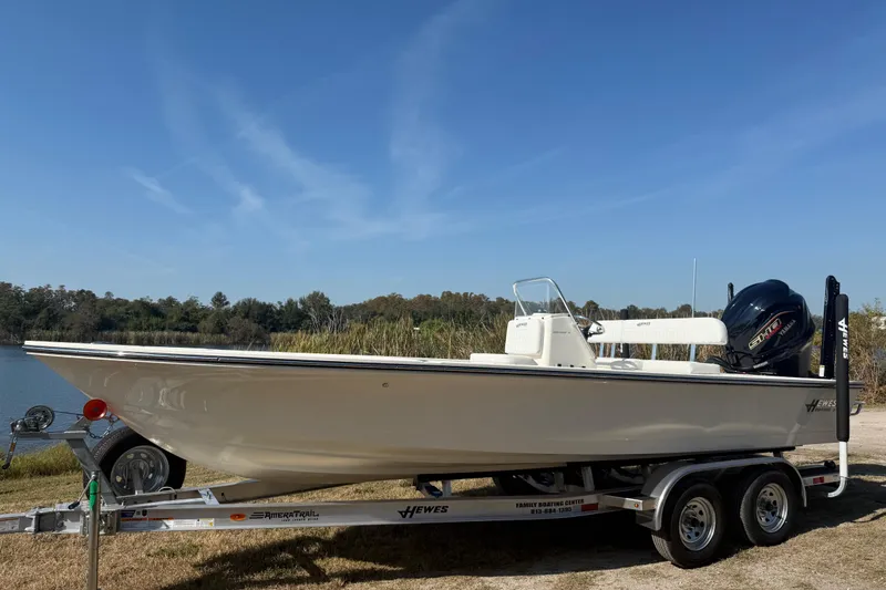 The Image of 2026 Hewes 21 REDFISHER boat on trailer by a lake under clear blue sky. - 0